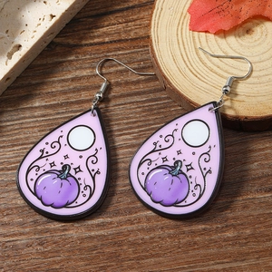 Detail of Halloween drop earrings with purple pumpkin motifs on a wooden background