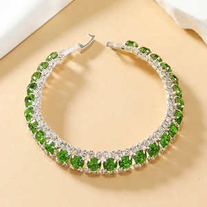 Gedetailleerde close-up van een zilveren tennisarmband met groene kristallen en strass