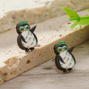 Dettaglio di orecchini a perno in legno a forma di pinguino con cappelli verdi e fiori