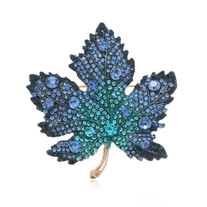 Eleganter Ahornblatt-Brosche mit blauen Kristallen und Goldbasis auf weißem Grund