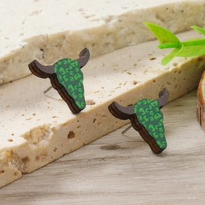 Dettaglio di orecchini a lobo in legno a forma di toro con stampa leopardata verde su marmo