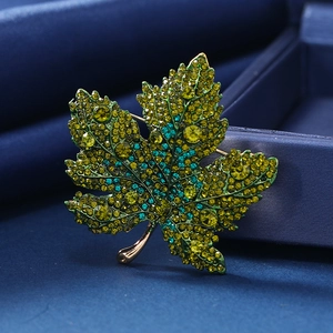 Broche de hoja de arce con cristales verdes brillantes sobre base de metal dorado