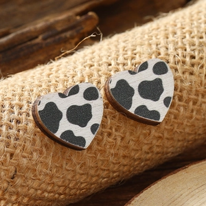 Macro shot of heart-shaped wooden stud earrings with a black and white cow print texture