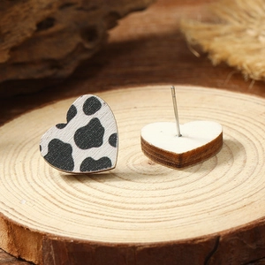 Close-up of heart-shaped wooden earrings featuring black and white cow print texture