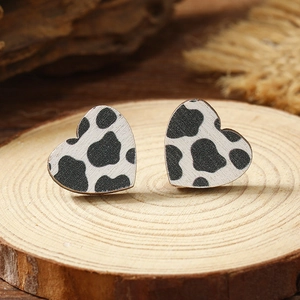 Macro shot of heart-shaped wooden earrings with black and white cow print on a rustic wood base