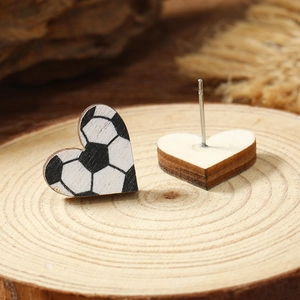 Macro view of heart-shaped wooden soccer earrings on a textured tree stump background