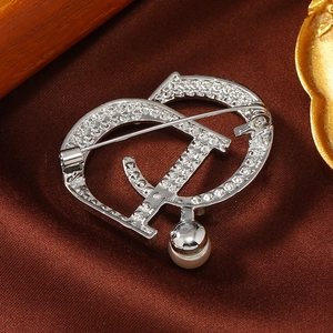 Macro detail of silver-tone CD letter brooch with sparkling rhinestones and pearl drop