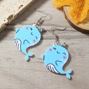 Close-up of blue acrylic narwhal earrings with cute cartoon faces on a wooden background