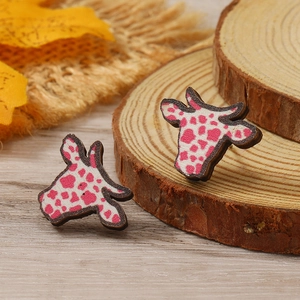 Detalle de pendientes de madera con forma de vaca y estampado rosa sobre fondo rústico