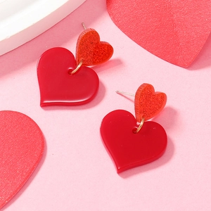Close-up of romantic red heart-shaped acrylic earrings on pink festive background