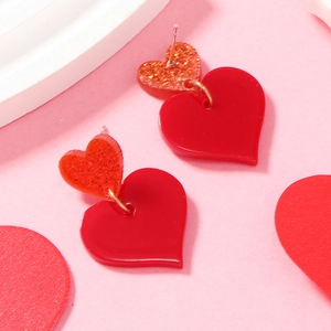 Detailed close-up of heart-shaped acrylic earrings with red glitter and matte finish