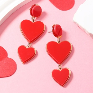 Detail of red acrylic heart-shaped drop earrings showing glossy layered design and metal rings