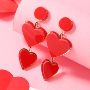Detail of red acrylic heart drop earrings with three-tier dangle design on artistic background
