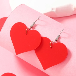 Detail shot of heart-shaped red acrylic earrings hanging on a pink curved display stand