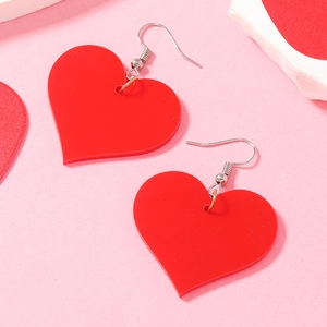 Detail of red heart acrylic drop earrings with silver hooks on a pink background