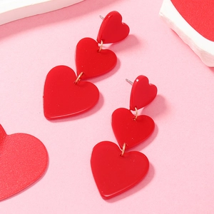 Detail view of triple red heart acrylic dangle earrings on a pink background