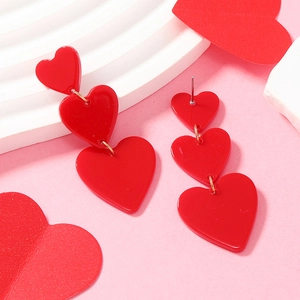 Close-up of stylish triple red acrylic heart drop earrings on a pink textured background