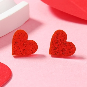Macro shot of red heart acrylic earrings with sparkling glitter and resin texture