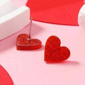 Macro view of heart-shaped red resin earrings with shimmering glitter and silver studs