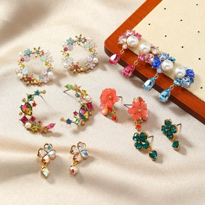 Chic floral stud earrings with pearls and colorful crystals on beige satin fabric background