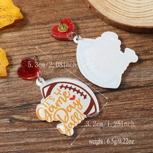 Detailed shot of leopard heart football earrings with It's Game Day text on wood