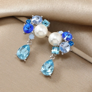 Detailed macro view of blue crystal cluster earrings with pearls on champagne silk fabric