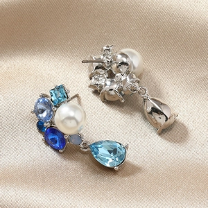 Close-up of silver earrings with white pearls and blue crystals on champagne silk fabric