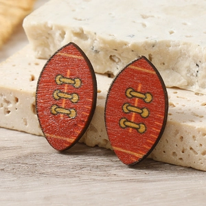 Macro detail of wooden rugby ball earrings with red-brown finish and yellow stitching