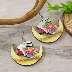 Detail van gele halve maan oorbellen met bloemenkonijn patroon op houten ondergrond
