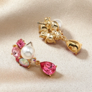 Detail of floral stud earrings with pink crystals and white pearl on golden satin