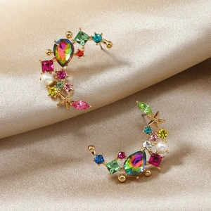 Detailed macro view of gold earrings with rainbow crystals and pearls on silk