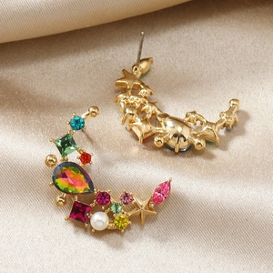 Macro shot of gold moon-shaped stud earrings with colorful crystals and pearls on silk