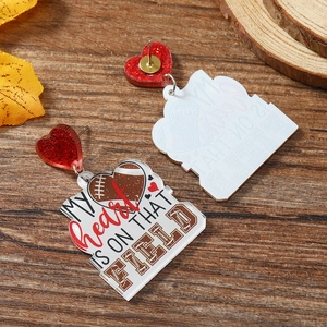 Macro detail of acrylic rugby earrings with My Heart Is On That Field text and red heart studs