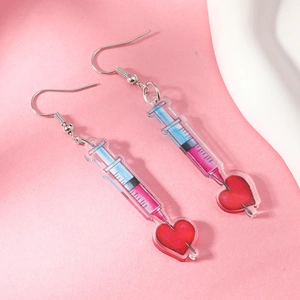 Detailed close-up of creative acrylic syringe earrings with heart charm on pink background