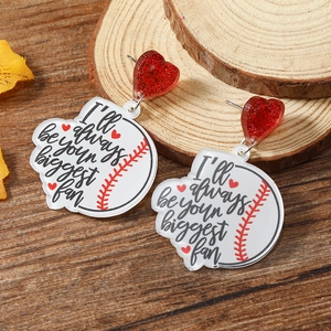 Detailed close-up of acrylic heart and baseball fan earrings on a natural wood surface