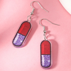 Close-up of creative capsule earrings with red and glittery purple acrylic texture