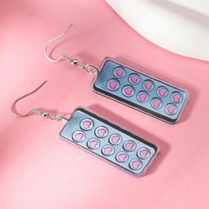 Macro detail of Y2K acrylic earrings with pink heart patterns and shimmering purple base