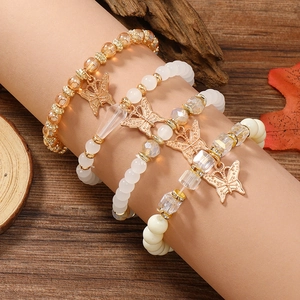 Detail eines vierteiligen Perlenarmband-Sets mit Schmetterlingsanhängern am Handgelenk