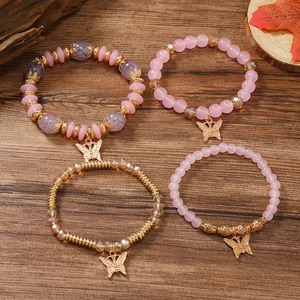 Detail eines vierteiligen Perlenarmband-Sets mit goldenen Schmetterlingsanhängern auf Holz