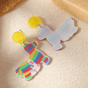 Detail van acryl regenboog piñata oorbellen met gele knopjes op getextureerde achtergrond