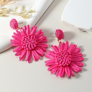 Detail of rose red woven raffia sunflower earrings on a natural textured background