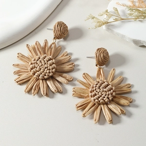Detail of woven raffia sunflower earrings with silver pins on a white stone background