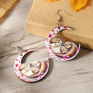 Detail of wooden crescent moon earrings featuring a cute mother and baby otter illustration