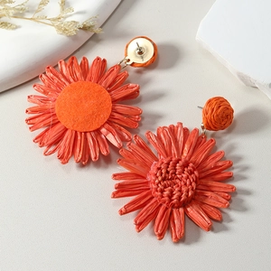 Macro detail of handmade orange raffia sunflower earrings with natural woven texture
