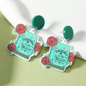 Détail de boucles d'oreilles livre et rose avec texte Reading is my Therapy sur acrylique
