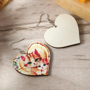 Close-up of heart-shaped wooden earrings featuring colorful cat illustrations on desk