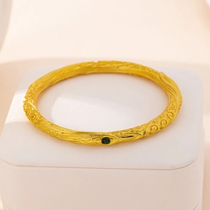 Vintage gouden armband met wolkenpatronen en een groene zirkoon in een luxe sieradendoos