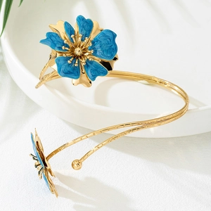 Golden flower arm cuff with blue enamel floral details on white ceramic tray