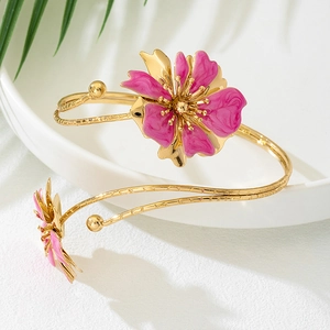 Detail view of a golden spiral arm cuff featuring a delicate pink enamel flower design