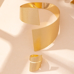Dettaglio del set bracciale rigido e anello dorati minimalisti con trama opaca
